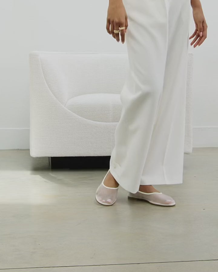 Model walking in Dear Frances Balla Mesh ballet flats in white, worn with wide-leg white trousers
